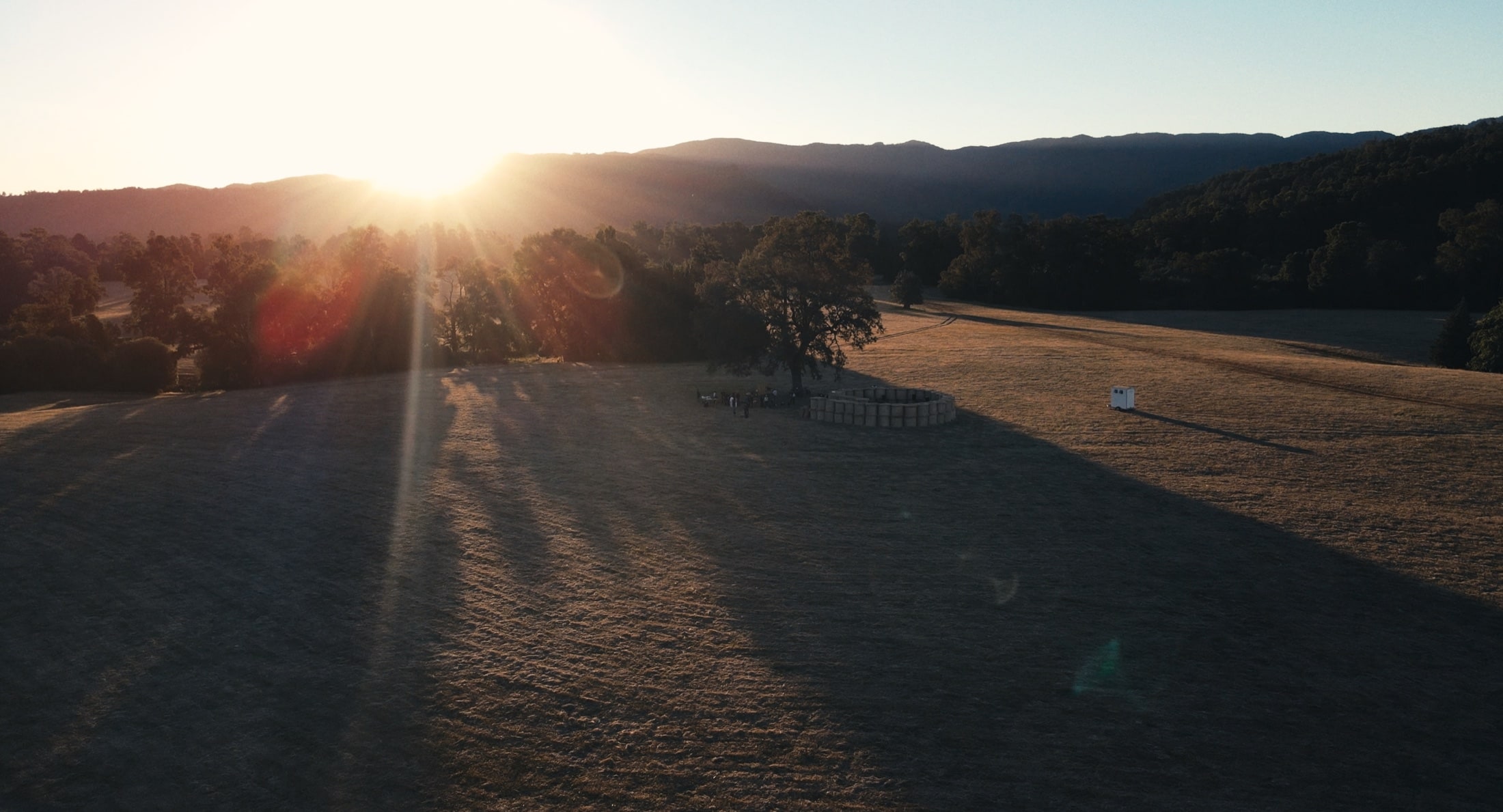 Aerial view of sunrise over an open field bordered by trees